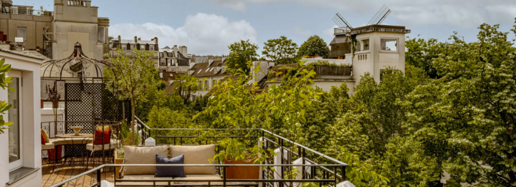 Terraço com sofá e vista para árvores, telhados e um antigo moinho ao fundo